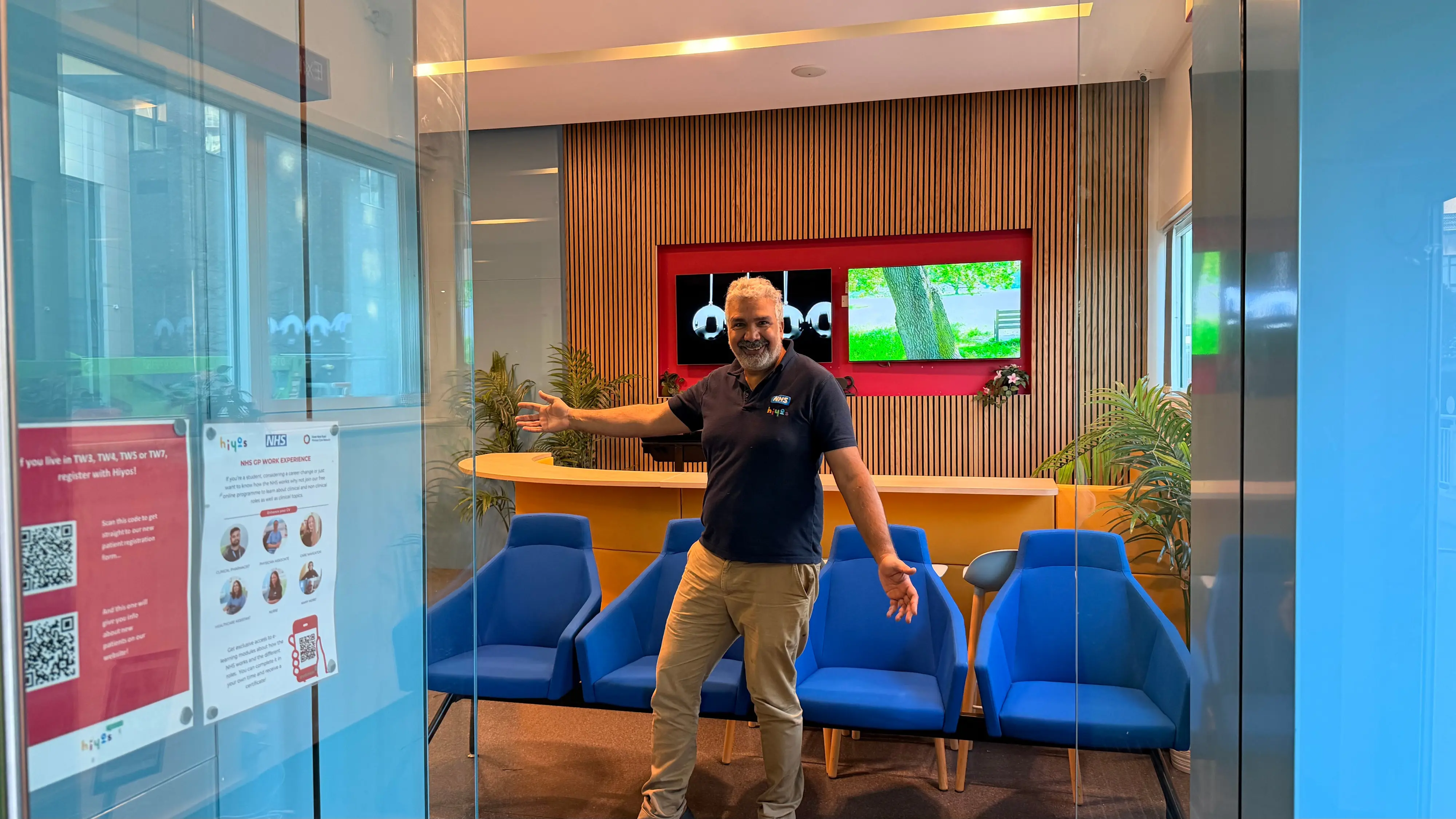 A GP welcoming people into a colourful waiting room.
