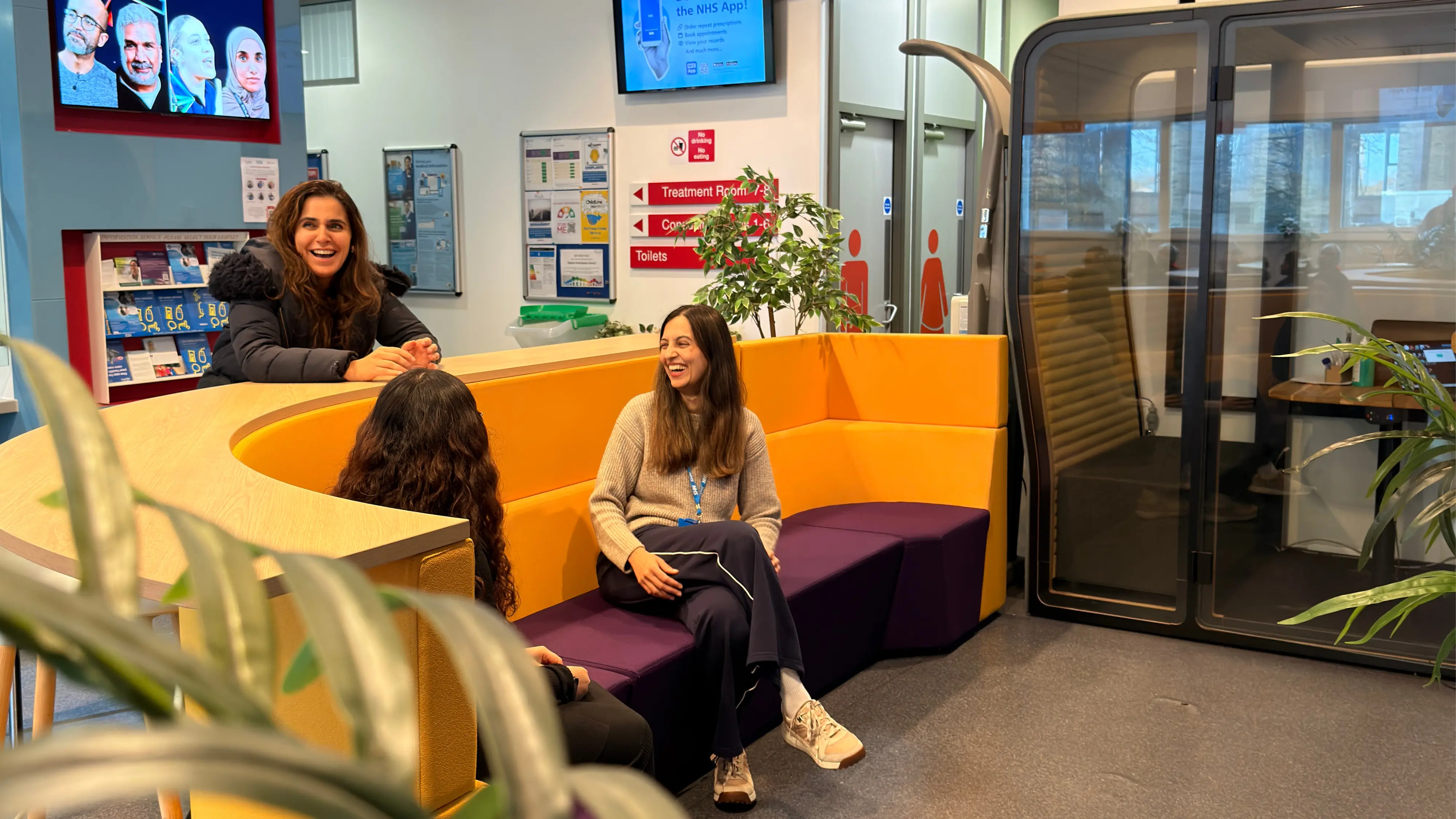3 women in a colorful waiting room in a GP practice. They are doing a group patient consultation